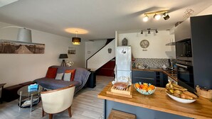 Un espace de vie compact comprenant un coin cuisine, un canapé, une table à manger avec des fruits et un escalier.