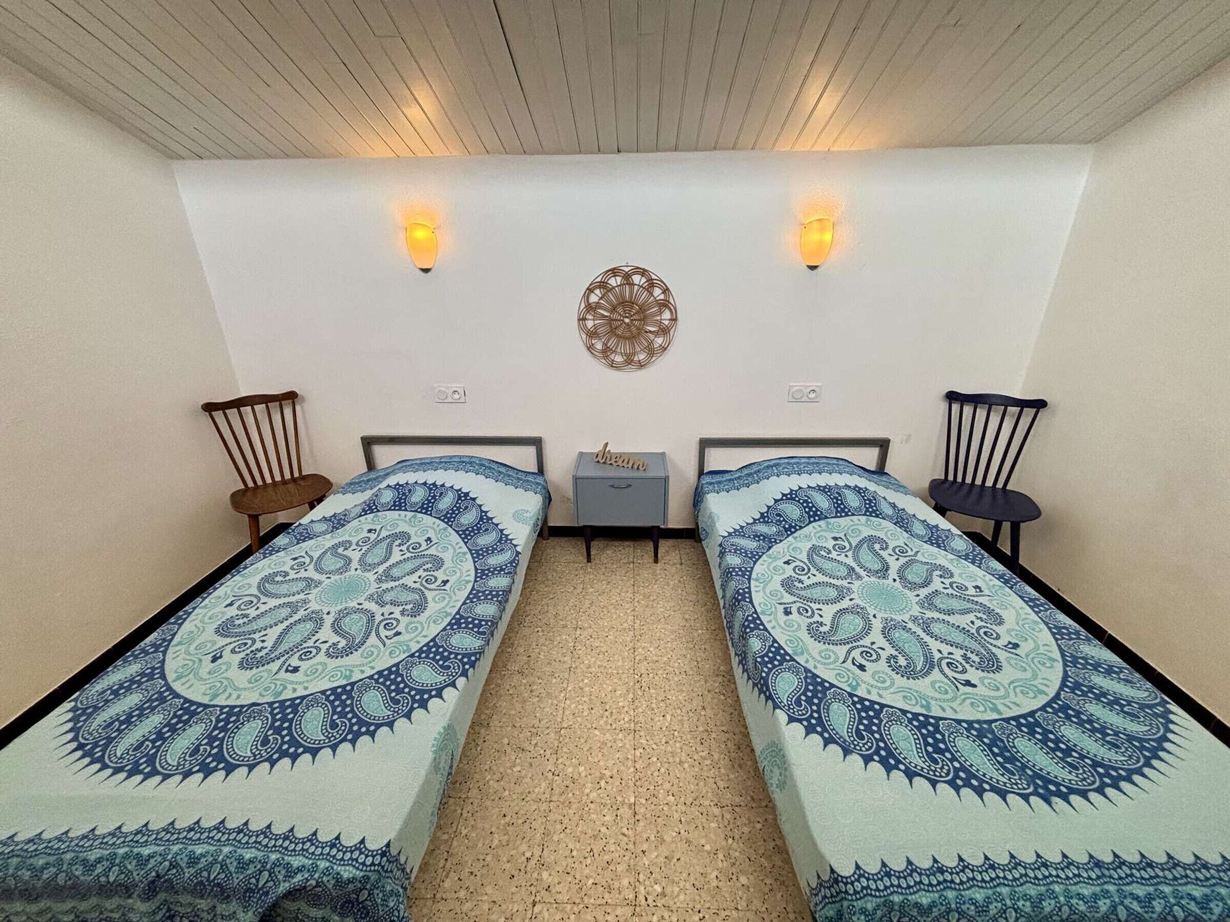 Ein Zimmer mit zwei Betten, einem kleinen Tisch, zwei Stühlen und Wandleuchten.