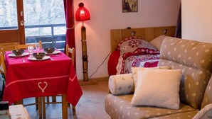 Ein gemütliches Zimmer mit einem Essplatz für zwei Personen, einem Holz-Kopfteil und einer Couch mit gemusterten Kissen.