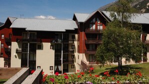 Ein Hotel mit mehreren Balkonen, einer rot-weißen Fassade und einer Bergkulisse.