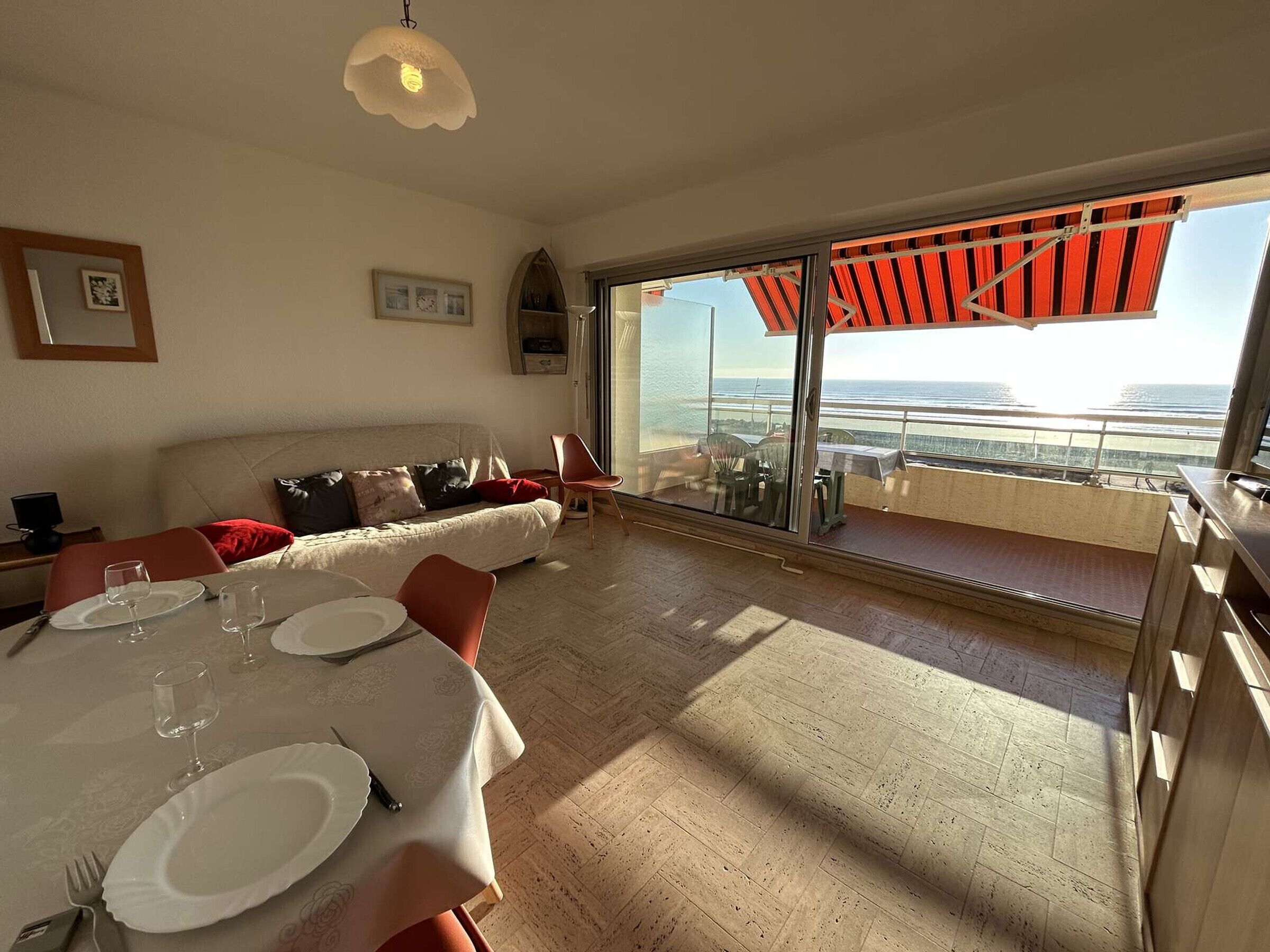 Uma sala de jantar com uma mesa posta para dois, um sofá e vista para o mar através de grandes janelas.