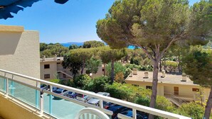 Un balcón con vista a una piscina, coches aparcados y edificios circundantes.