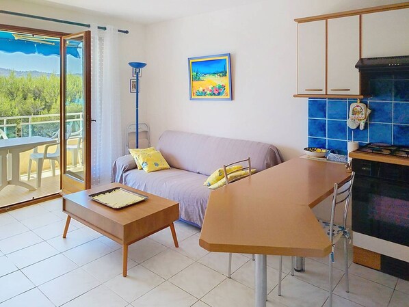 A living room with a sofa, a coffee table, a dining table, and a kitchen area with blue tiles.