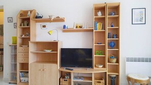 Una sala de estar con televisión, estantes de madera, una lámpara y una cesta de mimbre.