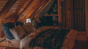 A cozy attic bedroom with a slanted ceiling, a bed with patterned bedding, a small table, and a window with curtains.
