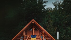 A wooden cabin with a balcony, surrounded by dense forest.