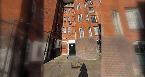 Une ruelle étroite, bordée de bâtiments en briques rouges, avec une porte centrale et une structure circulaire en briques.