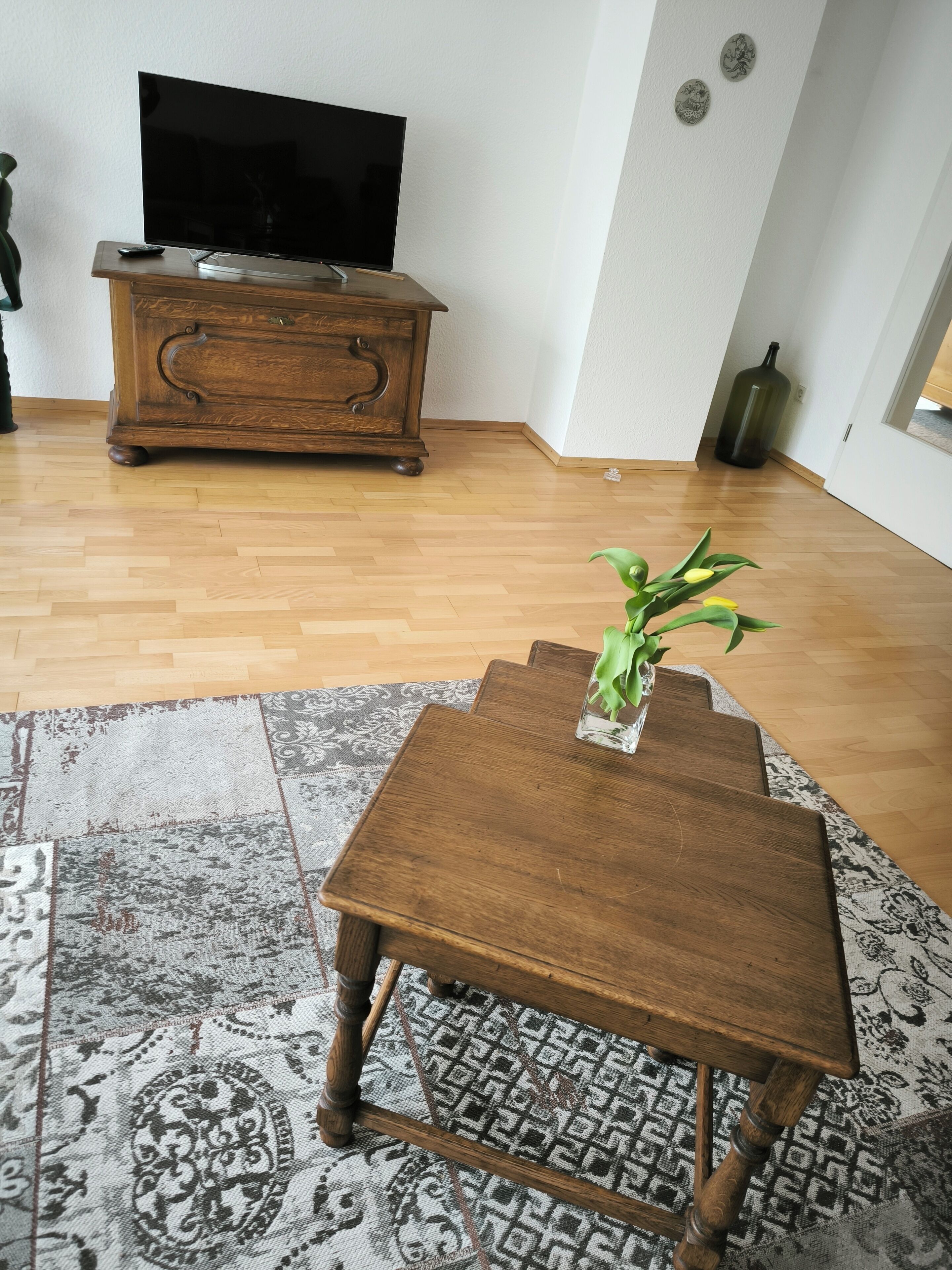 A living room with a wooden coffee table, a television on a wooden cabinet, and a patterned rug.
