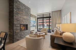 A modern living room with a stone fireplace, comfortable seating, a large window with a view, and a well-lit space.