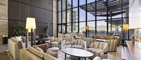 Amplia sala de estar con sofás, sillones y una mesa de centro, con ventanas grandes y vistas a la ciudad.