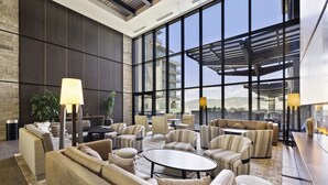 A spacious lounge area with sofas, armchairs, and a coffee table, featuring large windows and a view of the cityscape.