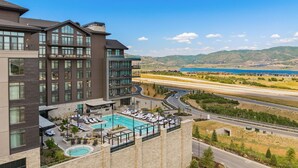A hotel with a rooftop pool, multiple floors, and a view of a highway and mountains.