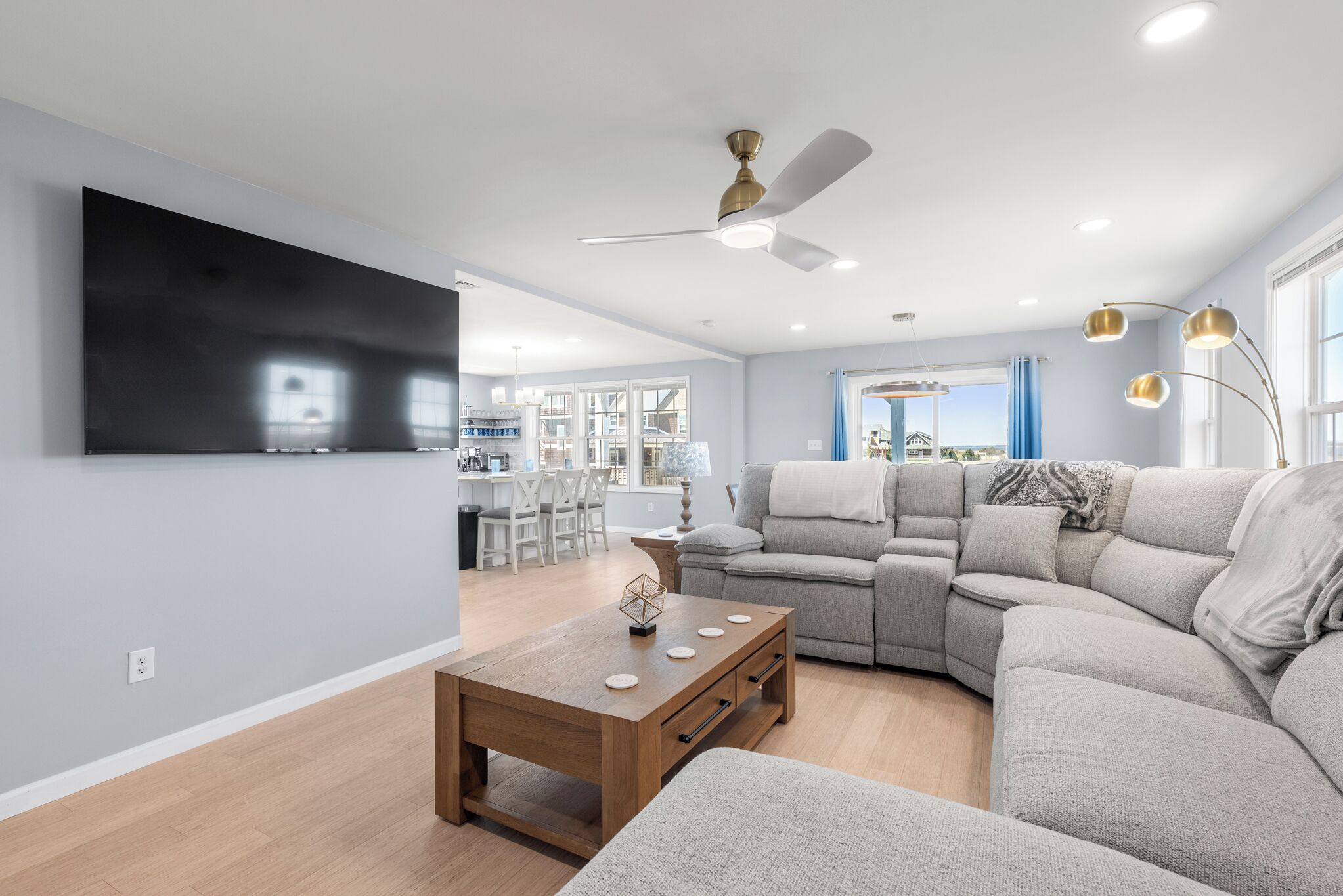 A modern living room with a sectional sofa, a wooden coffee table, and a flat-screen TV mounted on the wall.