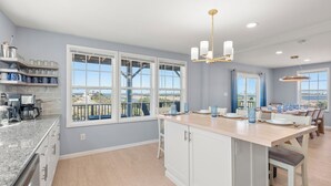A modern kitchen with a large island, white cabinetry, and a view of the outdoors through large windows. - Bela Vista: Stunning Water Views, Hot Tub, Pets OK (Nags Head)
