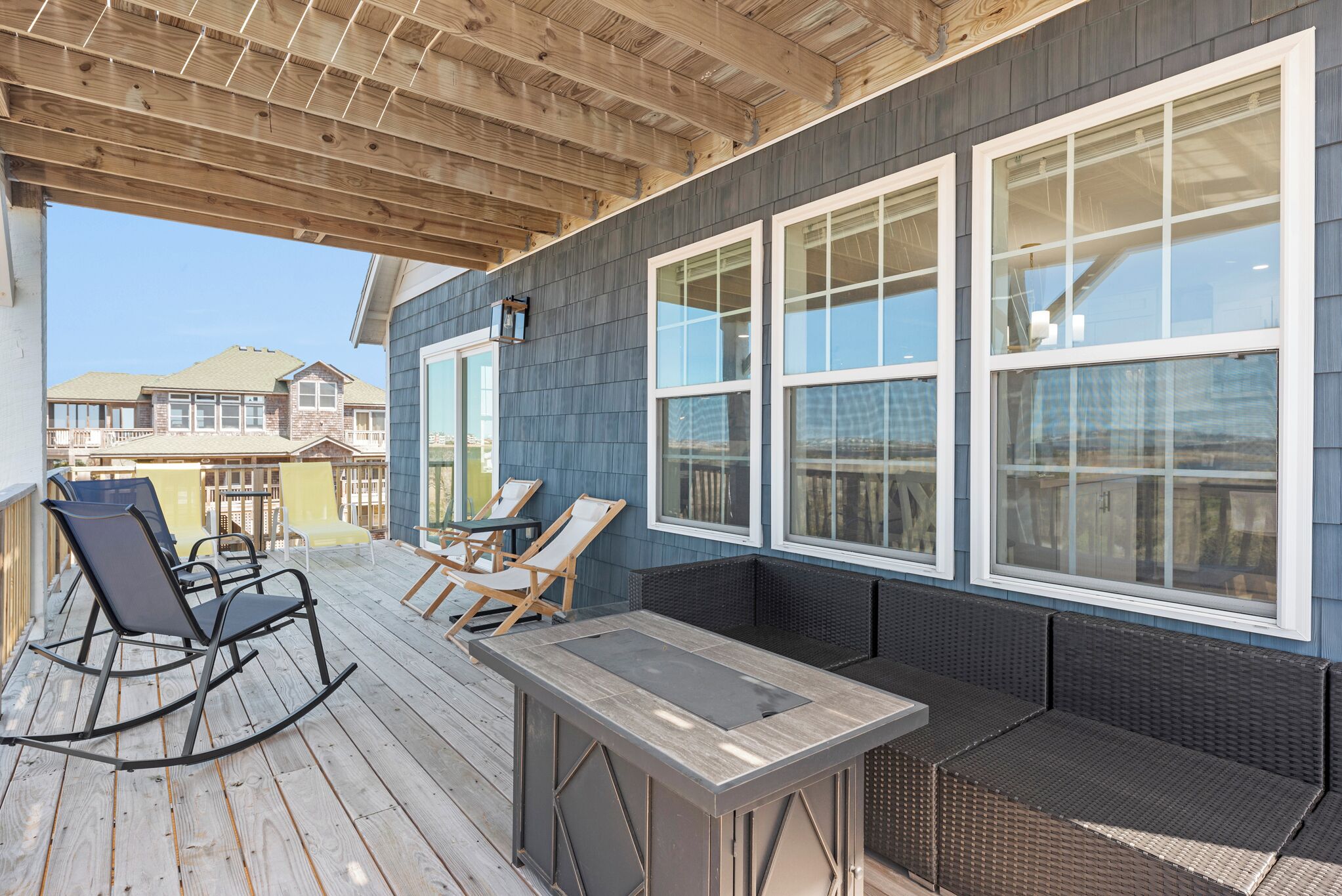 A covered outdoor seating area with a table and chairs, a pergola overhead, and large windows.