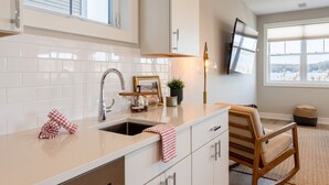 Een moderne keuken met witte kastjes, een roestvrijstalen spoelbak en een houten stoel.