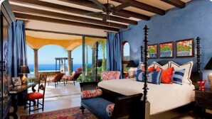 Une chambre à coucher avec un lit à baldaquin, une vue sur la mer et un balcon avec des sièges d’extérieur.