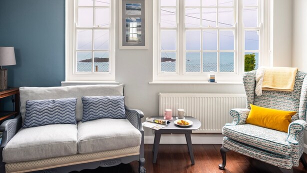 A cozy room with a sofa, armchair, and a small table with a cup and plate. - Stylish Dog-Friendly Cottage with Stunning Sea Views in Mousehole, secure garden (Mousehole)