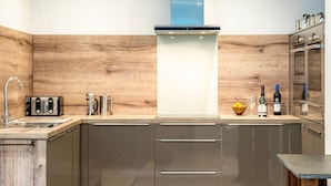 A modern kitchen with wooden accents, stainless steel appliances, and a built-in oven. - Stylish Dog-Friendly Cottage with Stunning Sea Views in Mousehole, secure garden (Mousehole)
