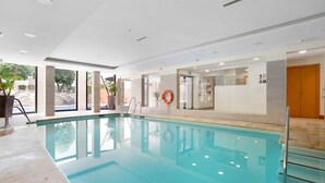 Una piscina con agua cristalina, rodeada por un solado de baldosas y paredes interiores.