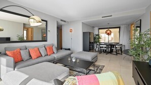 Una sala de estar moderna con un sofá seccional gris, una mesa de centro y una zona de comedor con una mesa redonda y sillas.