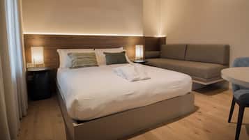 Una habitación de hotel moderna con una cama grande, un sofá, una mesa redonda y una mesita de noche con lámpara.