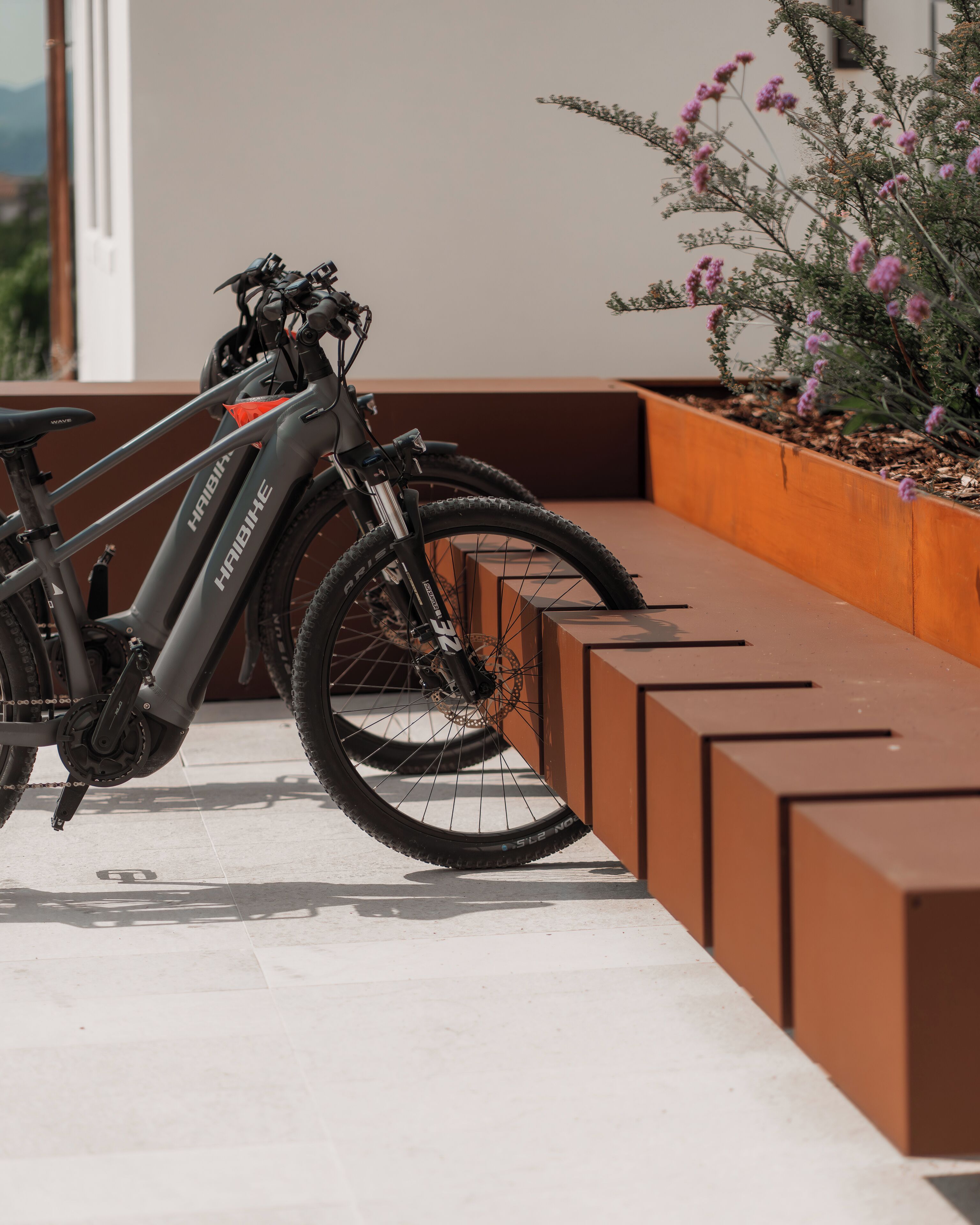 A stationary electric bike parked next to a modern outdoor seating area with a planter of flowers.