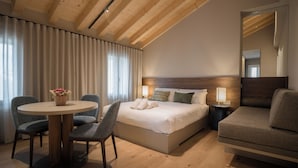 A hotel room with a wooden ceiling, a bed with white linens, a round table with two chairs, and a sofa. - Agriturismo Pra' dell'Ort (Valdobbiadene)
