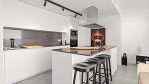 A modern kitchen with white cabinetry, a central island with stools, and a red decorative element. - RDR467 - Luxury penthouse with sea view rooftop (Estepona)