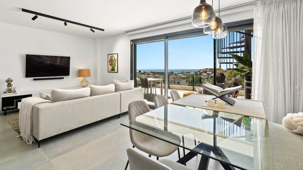 A modern living room with a sofa, glass dining table, chairs, a TV, and a large window with a view. - RDR467 - Luxury penthouse with sea view rooftop (Estepona)