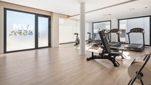 Un'ampia palestra con tapis roulant, cyclette e vogatore. Grandi finestre offrono luce naturale e vista sulla città.