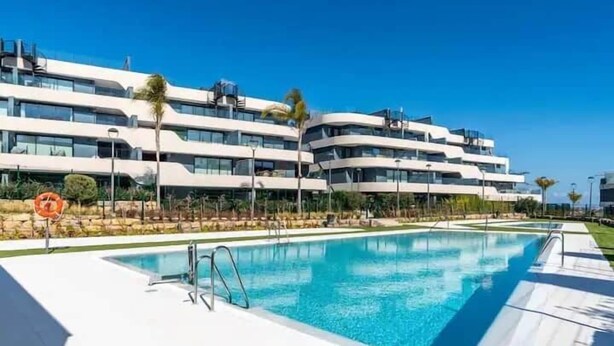 Un hotel moderno con piscina, diversi balconi e un cielo azzurro limpido.