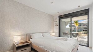 Camera da letto moderna con un letto grande, un comodino e una scrivania. C'è una porta scorrevole in vetro che dà su un balcone con mobili da esterno.