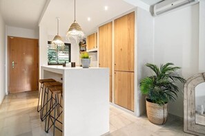 Une cuisine moderne avec des meubles en bois, un îlot central doté de tabourets, un éclairage suspendu et une plante en pot.