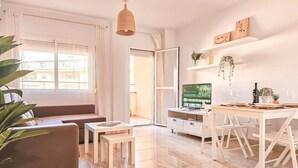 En moderne stue med sofa, spisebord med stole, fjernsyn og en plante.
