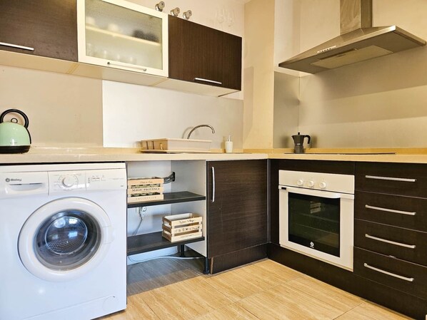 A compact kitchen with a washing machine, a built-in oven, and a coffee maker.