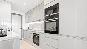 Une cuisine moderne avec des meubles blancs, un four encastré, un four à micro-ondes et un grille-pain.