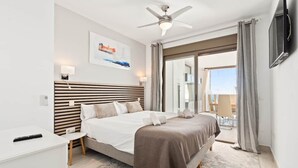 Une chambre d’hôtel moderne dotée d’un grand lit, d’un ventilateur de plafond, d’une télévision et d’un balcon avec des rideaux.
