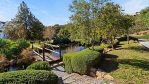 Un jardin avec un pont en bois, un étang et diverses plantes.
