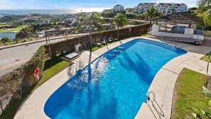 Une piscine à bordures courbes, entourée d’un petit muret et agrémentée d’une petite terrasse avec des chaises longues.