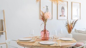 Mesa redonda de comedor con un jarrón rosa, vasos transparentes y platos para cuatro.