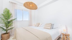 Un dormitorio con una cama grande, una lámpara colgante, una planta en maceta y una mesita de noche con lámpara.