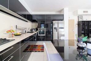 A modern kitchen with black cabinets, stainless steel appliances, and a colorful rug. - MAMAD Stunning 2BR/2BA SeaView Apt| By SweetyGuest (Tel Aviv-Yafo)