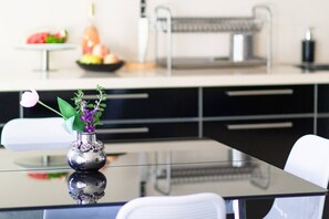 A modern kitchen with a reflective black table, a vase with flowers, and a fruit bowl in the background. - MAMAD Stunning 2BR/2BA SeaView Apt| By SweetyGuest (Tel Aviv-Yafo)