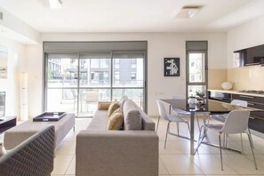 A modern living room with a sofa, dining table, chairs, and a kitchen area. - MAMAD Stunning 2BR/2BA SeaView Apt| By SweetyGuest (Tel Aviv-Yafo)