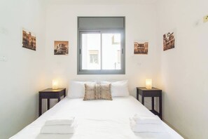 A bedroom with a large bed, two bedside tables with lamps, and a window with a view of buildings.