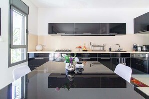 A modern kitchen with black cabinets, a central island, and a dining area with white chairs. - MAMAD Stunning 2BR/2BA SeaView Apt| By SweetyGuest (Tel Aviv-Yafo)