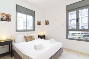 A hotel room with a large bed, two bedside tables, and two windows.