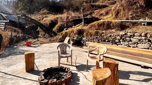 A concrete patio with a fire pit, two wooden chairs, and a rustic wooden table. - Apple velley homestay shanghar  (Sainj)