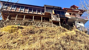 A multi-story building with a stone base, wooden balconies, and a red roof. - Apple velley homestay shanghar  (Sainj)